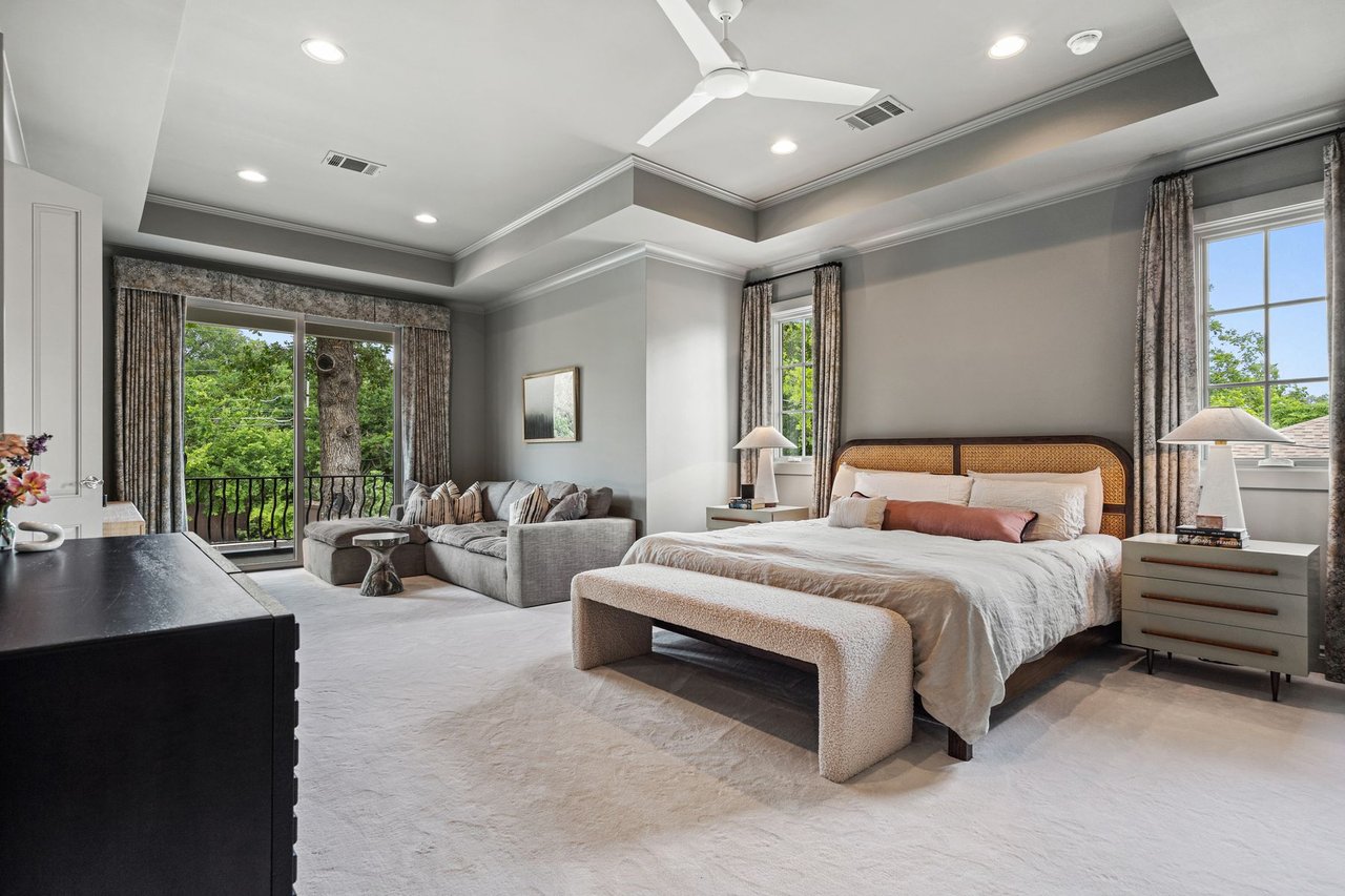 Primary bedroom with a tray ceiling, sitting area, and a private balcony overlooking the trees, furnished by Ashby Collective, at 2600 Westover Road in Tarrytown, Austin.