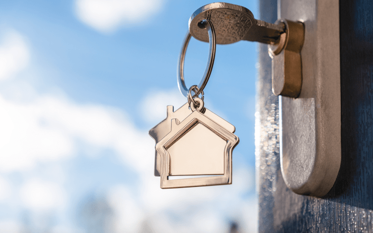 Close-up of house-shaped key on key ring in door lock. Symbolizes moving and home ownership.