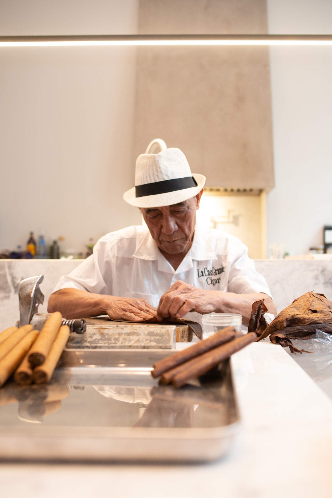 Cigar maker in a white hat rolling cigars at a workbench.