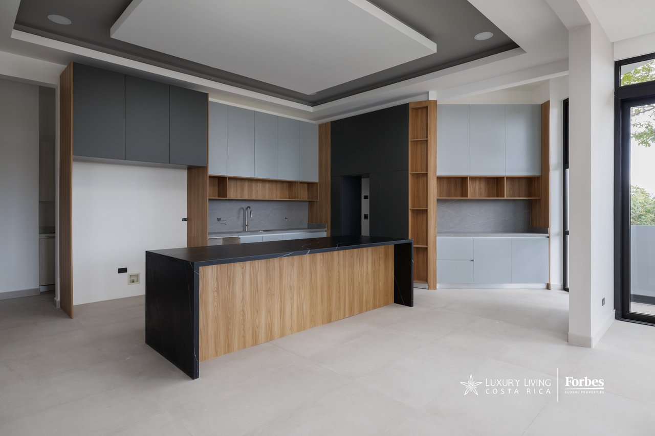 Modern apartment kitchen with a large wood-front island, black countertop, and gray cabinetry.