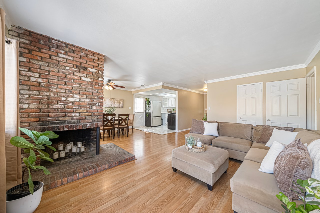 Living room with a brick fireplace, beige sectional sofa, and hardwood floors.