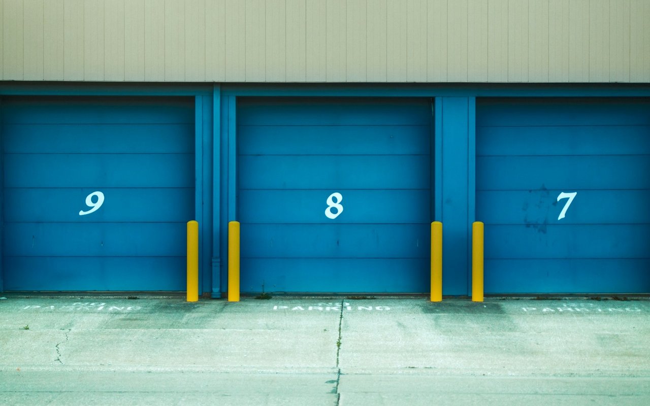 Blue self-storage doors numbered 9, 8, and 7, protected by yellow bollards.