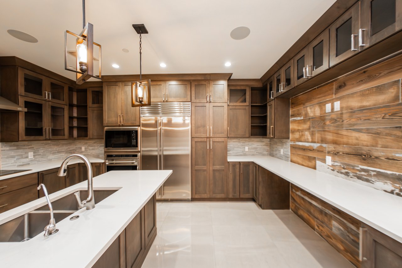 Luxury kitchen with dark wood cabinetry, stainless steel appliances, and a large white island with a double sink.