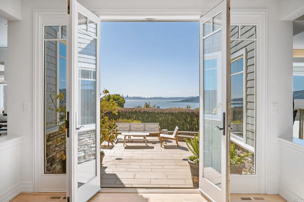 Open doors lead to a furnished stone terrace overlooking the bay and distant city skyline.