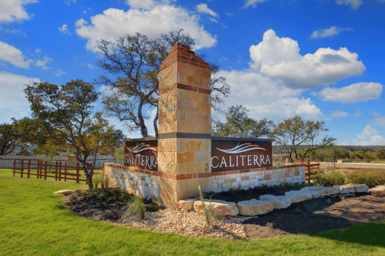 Caliterra neighborhood entrance sign with a stone pillar and red fencing.