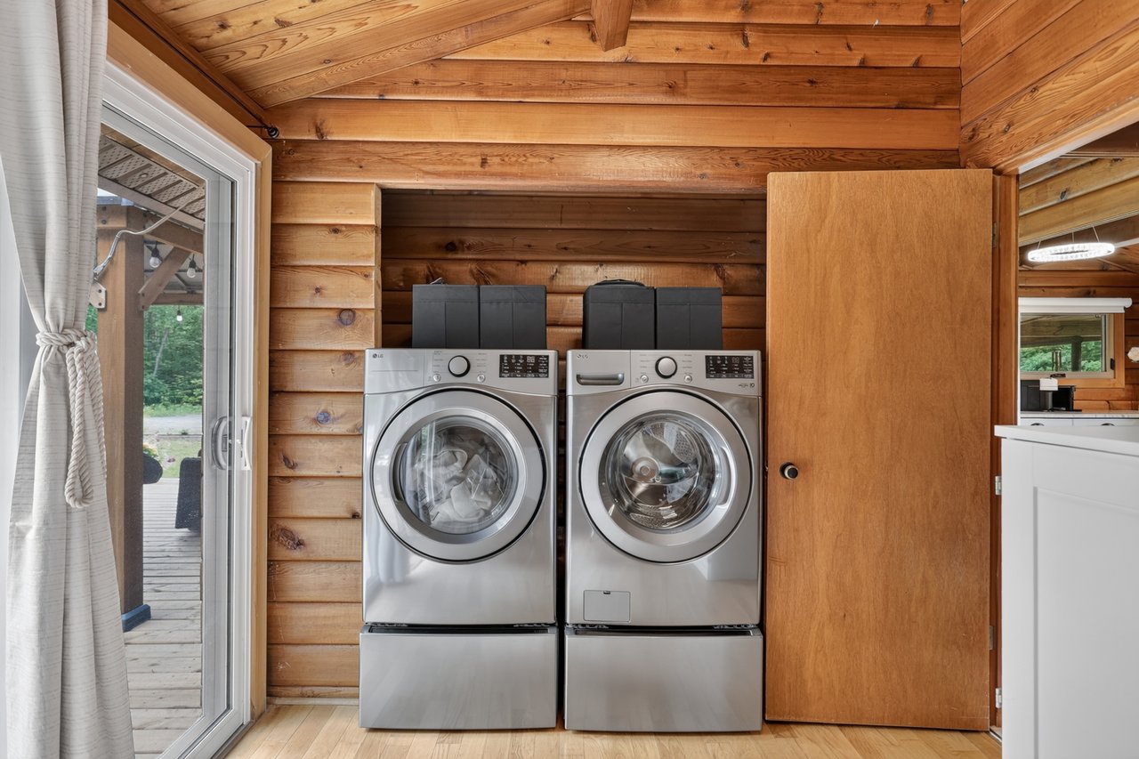 Laundry area with front-loading washer and dryer, log walls, and a glass door to the deck.
