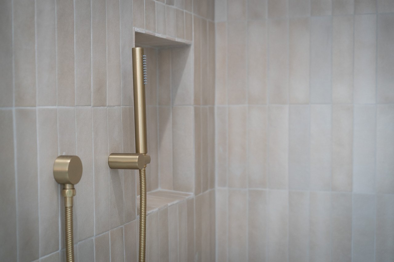 Bathroom shower with brushed brass fixtures and a recessed niche in beige tile.