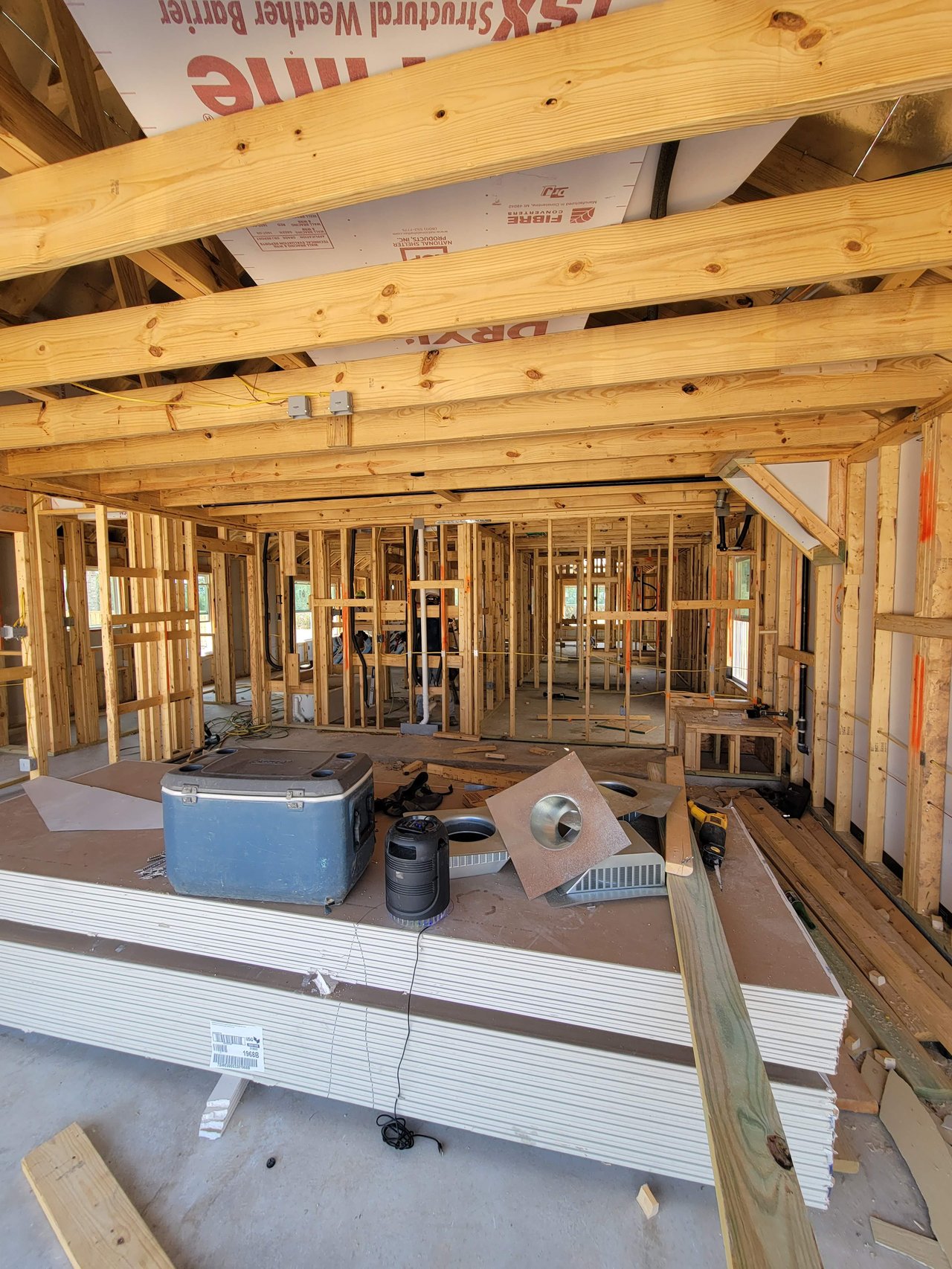 Unfinished house interior with exposed roof trusses, wall framing, and construction materials.