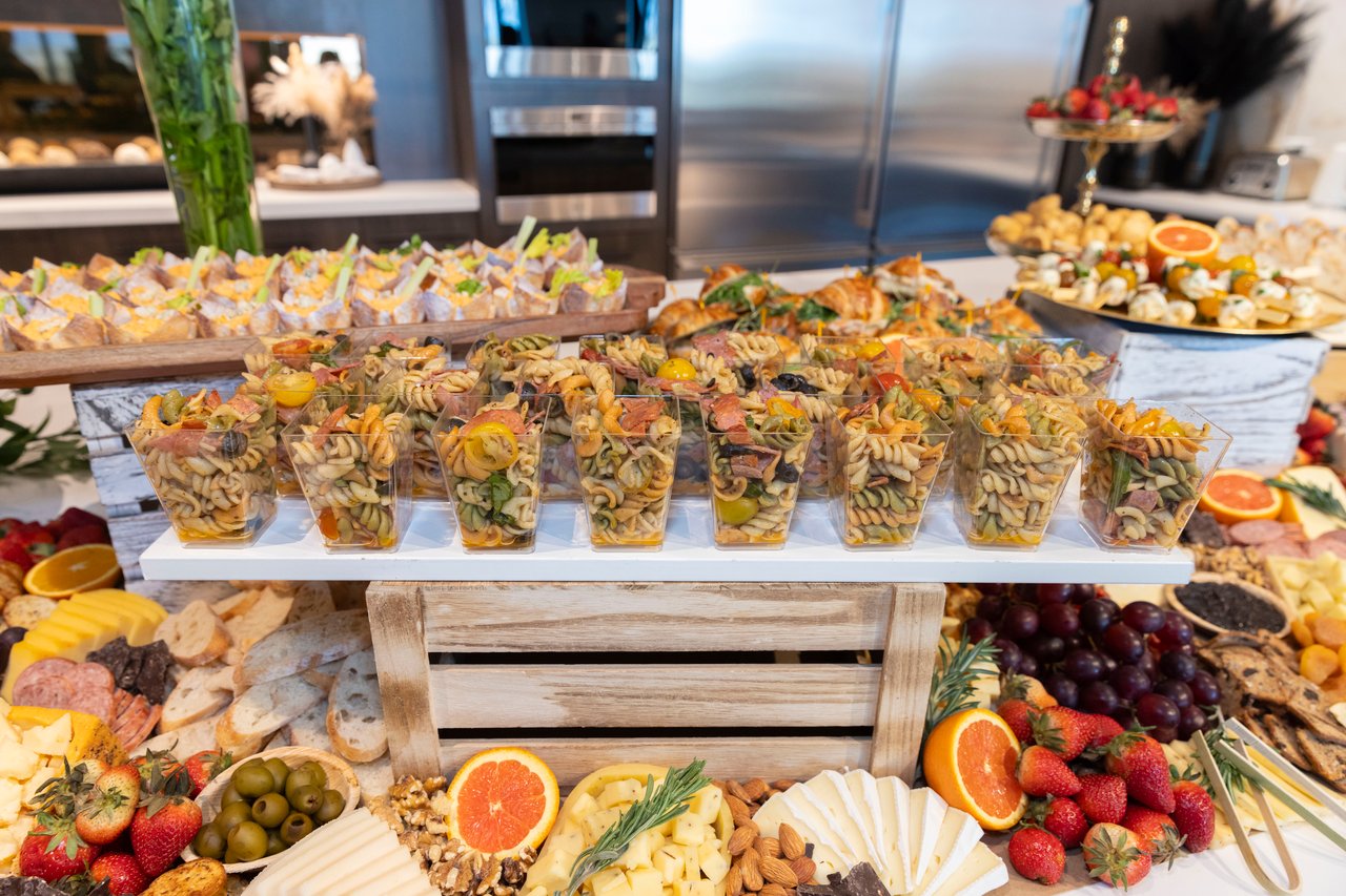 Buffet spread of pasta salad cups, sandwiches, cheese, and fresh fruit.