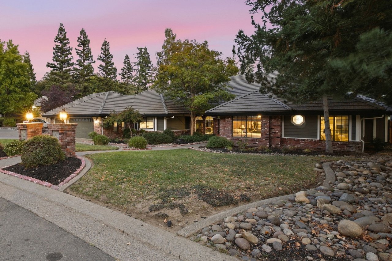 Single-story home with brick accents, a tiled roof, and a landscaped front yard at dusk.