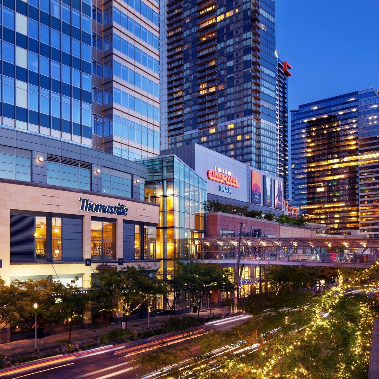 Downtown high-rises at dusk, with illuminated storefronts and a Cinemark IMAX theater.