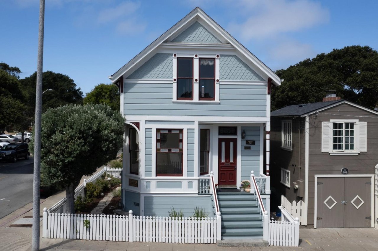 Light blue two-story house with a red front door and white picket fence.