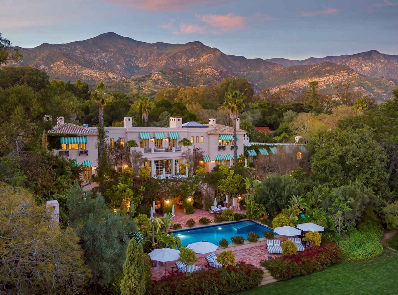 A mansion with a pool, lush trees, and mountains in the background