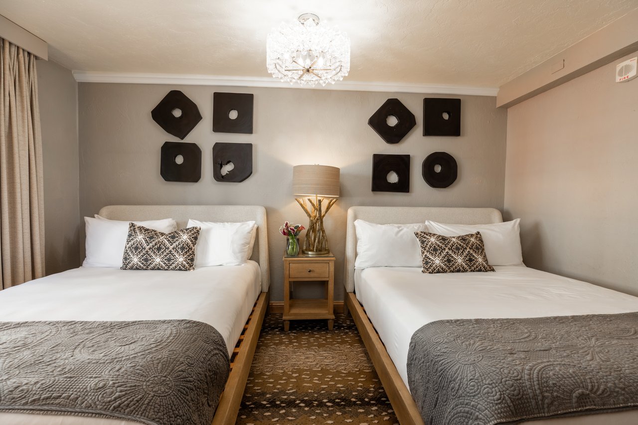 Bedroom with two white beds, a shared nightstand, geometric wall art, and a crystal chandelier.