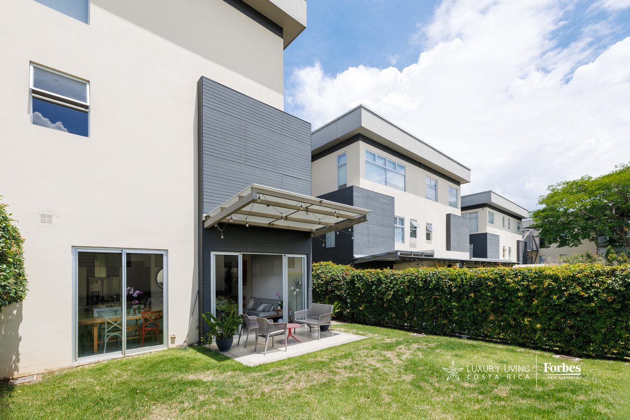 Modern townhouse rear exterior with covered patio, outdoor seating, and lawn.