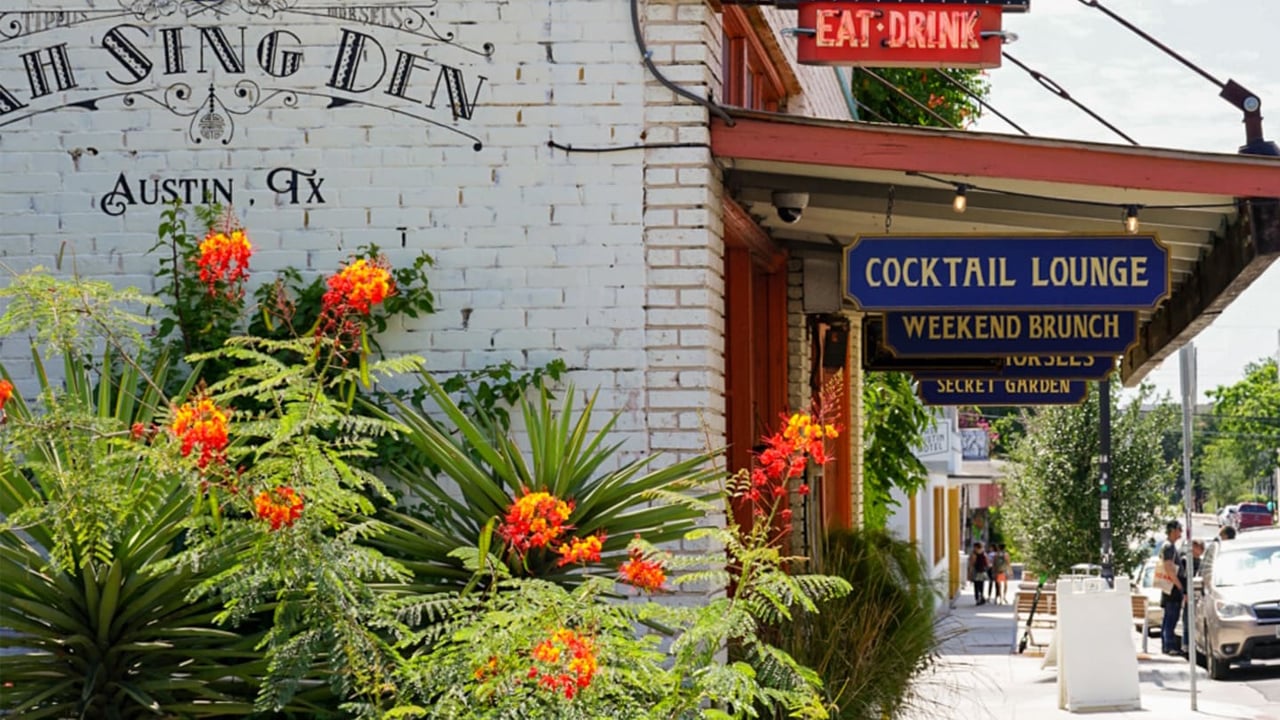 A sidewalk in front of a restaurant with a cocktail lounge and weekend brunch signs hanging from it in East Austin