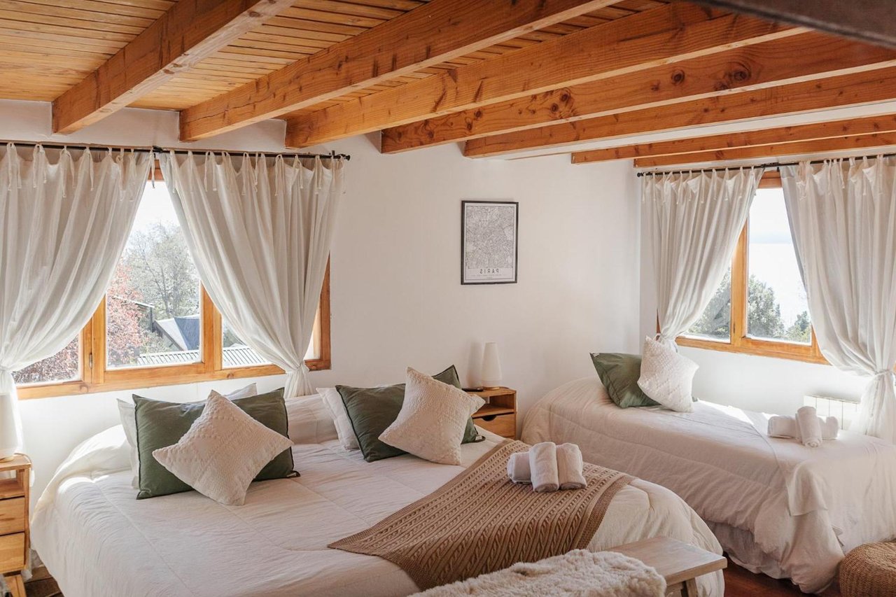 Boutique hotel bedroom with two beds beneath exposed timber ceiling beams and beside wooden-framed windows.