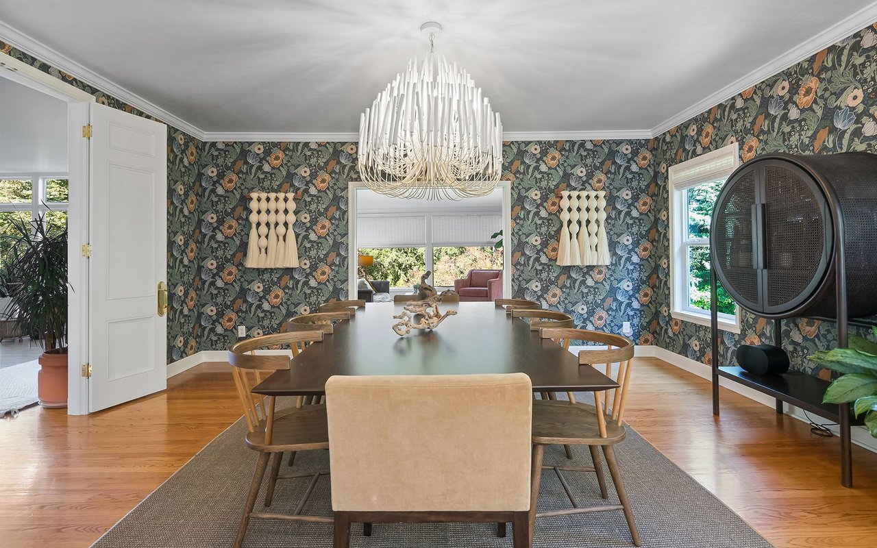 Dining room with floral wallpaper, a long table, wooden chairs, and a sculptural white chandelier.