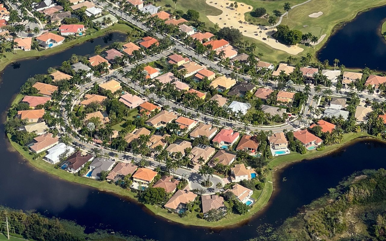 Aerial view of Isabela homes among palm trees, bordered by water and a golf course.