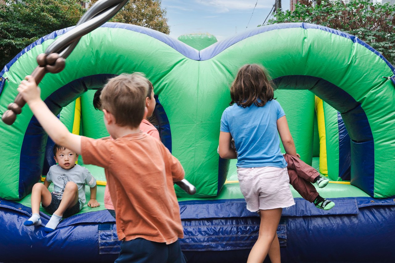 Children play and joust inside a green and blue inflatable bounce house.