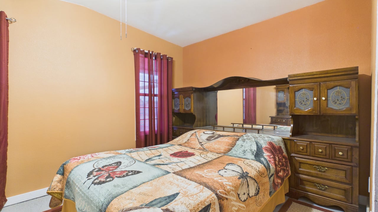 Furnished bedroom with a dark wood mirrored headboard and butterfly-patterned bedspread.