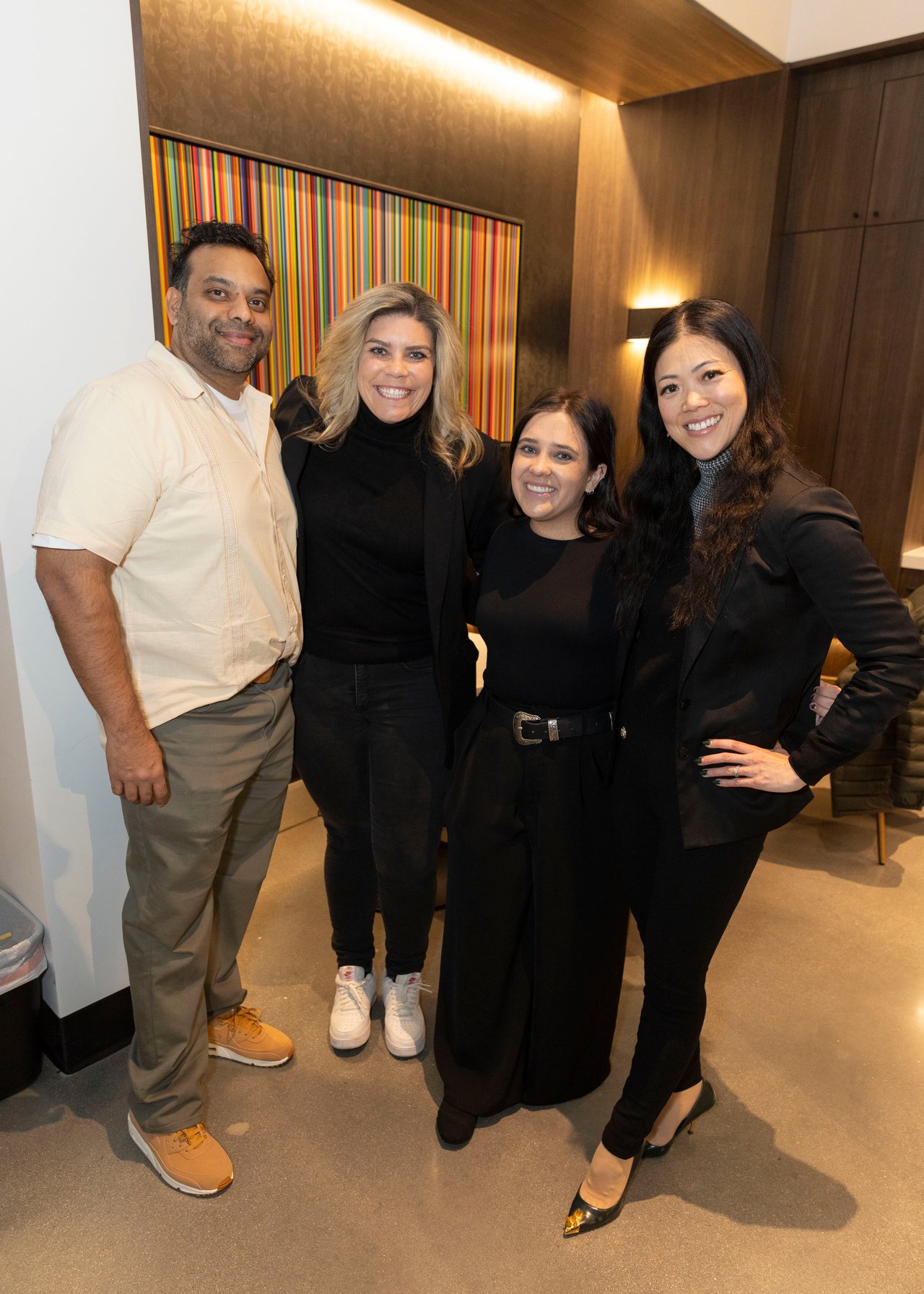 Four adults pose together at an open house in front of colorful striped artwork.