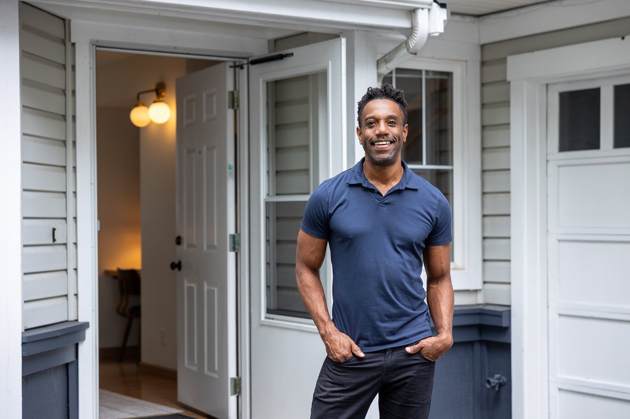 Smiling man in a navy polo standing beside the open front door of a home.