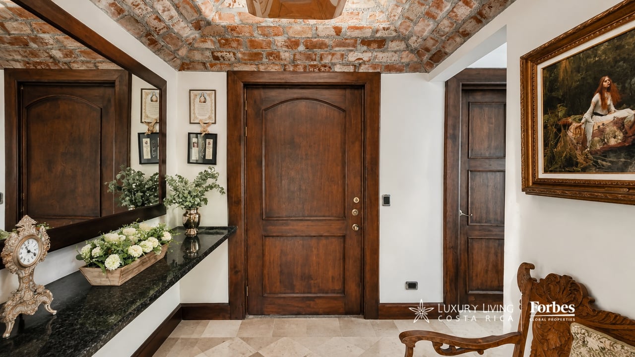 Entry foyer with dark wood doors, an exposed brick ceiling, and a flower-decorated console beneath a large mirror.