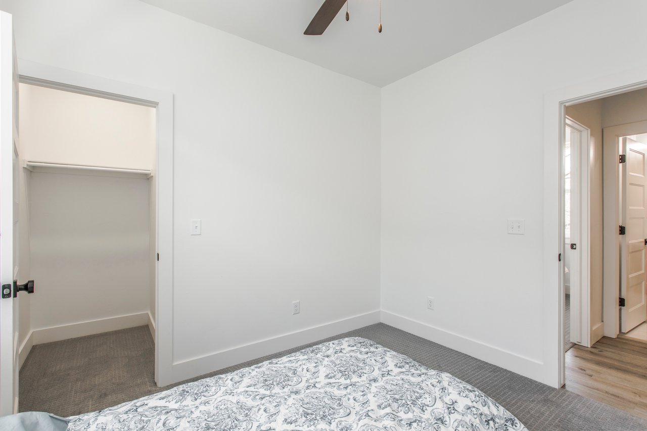 Bedroom with a patterned bedspread, gray carpet, and an open closet.