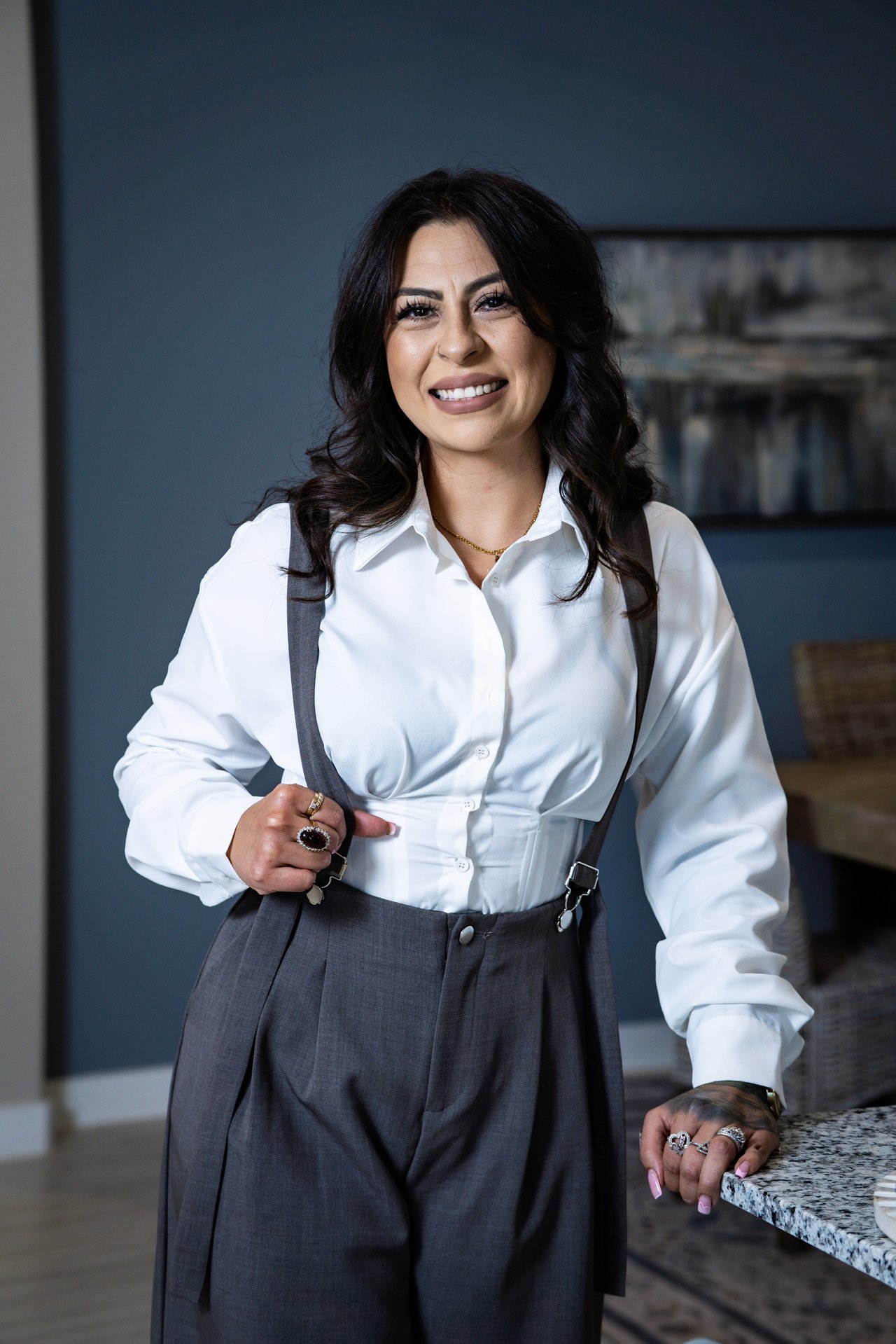 Sara Saenz smiling in a white blouse and gray trousers with suspenders.
