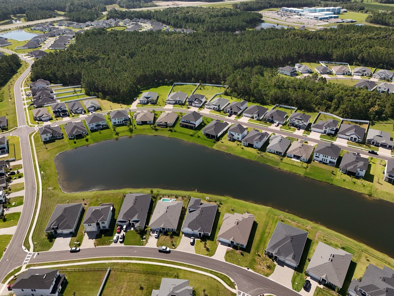 Aerial view of homes lining a pond in a green, wooded neighborhood.