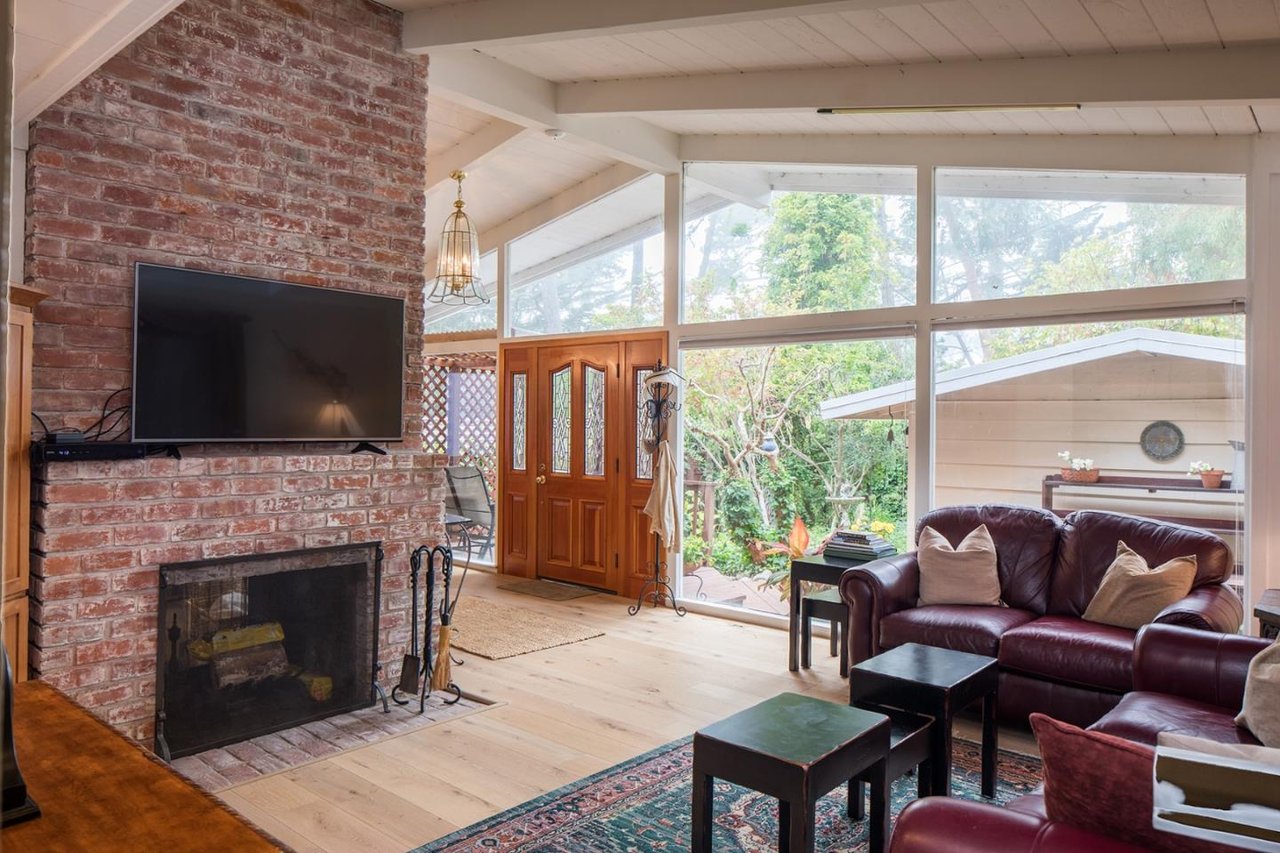 Living room with a brick fireplace, leather sofa, and large garden-facing windows.