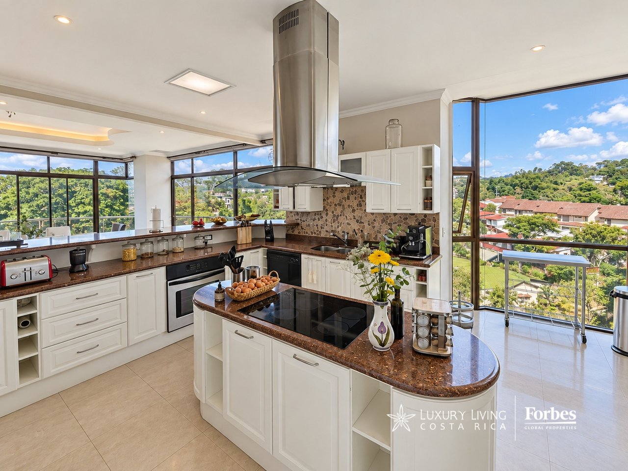 Penthouse kitchen with a large stone island, stainless steel range hood, and windows overlooking green hills.