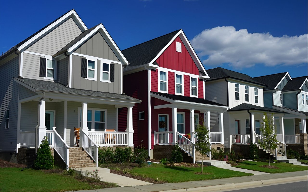 Closely spaced two-story homes with front porches, including a red house between gray neighbors.