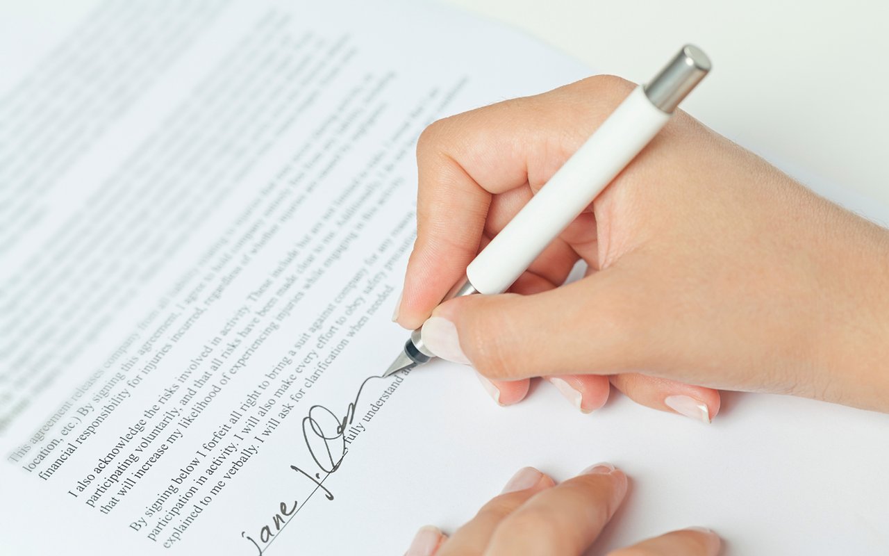 Hands sign a printed agreement with a white pen.