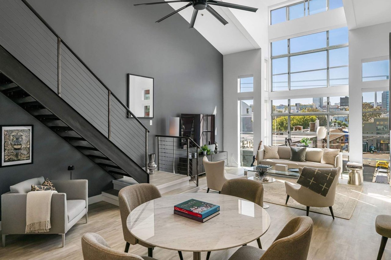 Modern living room with a black staircase, marble table, and tall windows overlooking the city.