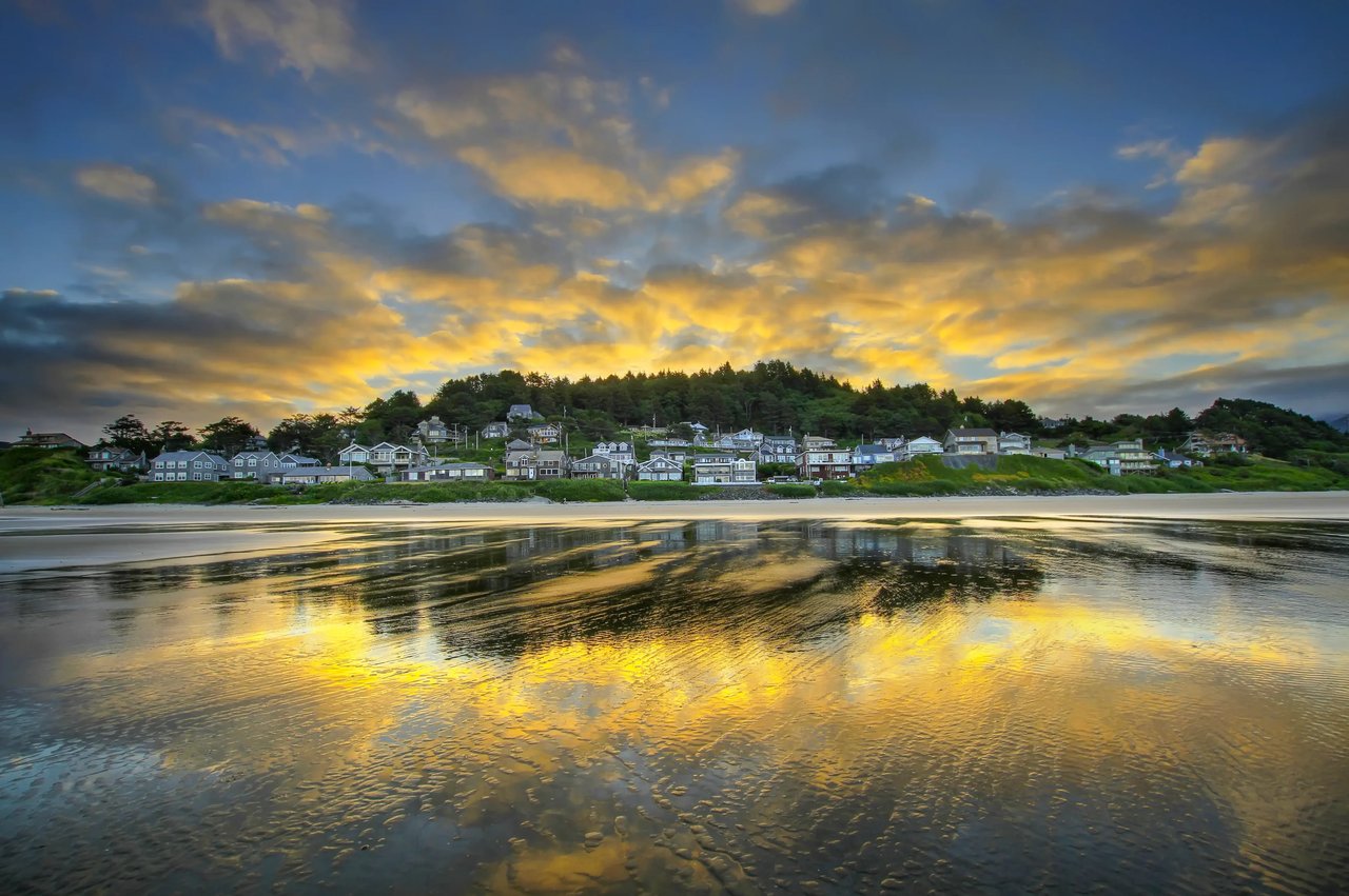 Sunrise clouds and homes on a hill with a reflection on the wet sand