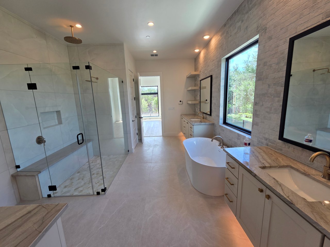Contemporary bathroom with a glass shower, freestanding tub, and double-sink stone vanity beside large windows.