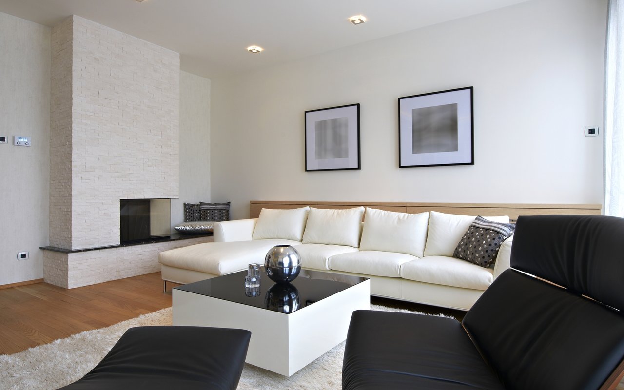 Modern living room with a white sectional, stone fireplace, and black leather lounge chairs.