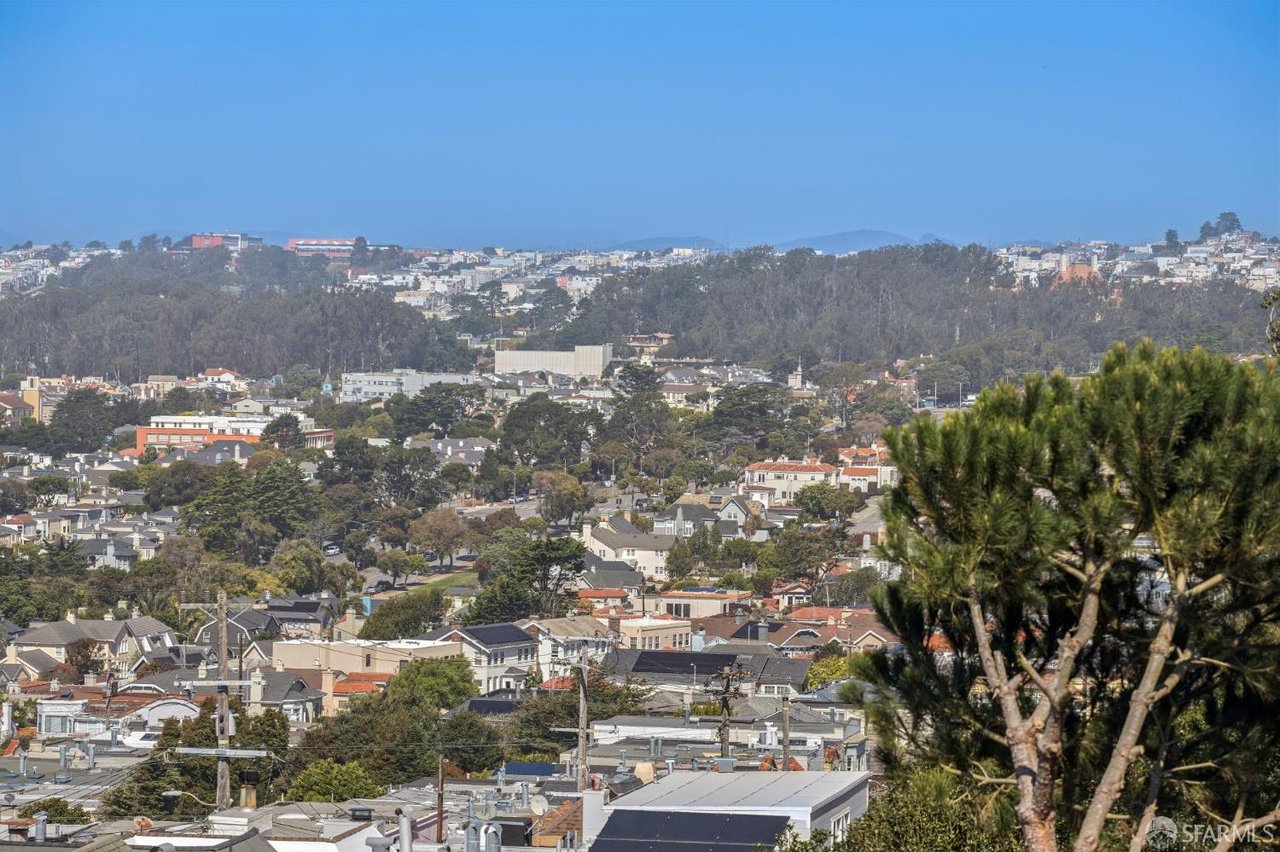 San Francisco neighborhood rooftops and wooded hills, viewed from above beneath a clear blue sky.