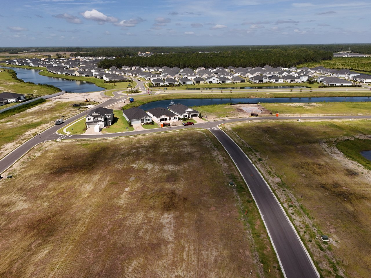 Aerial view of a developing neighborhood beside a waterway, with homes and cleared lots.