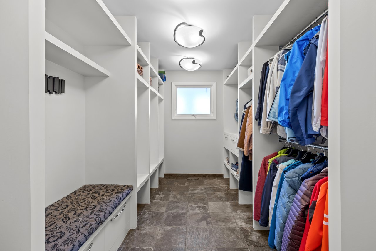 Walk-in closet with built-in shelving, a cushioned bench, tiled floor, and clothes hanging along one side.