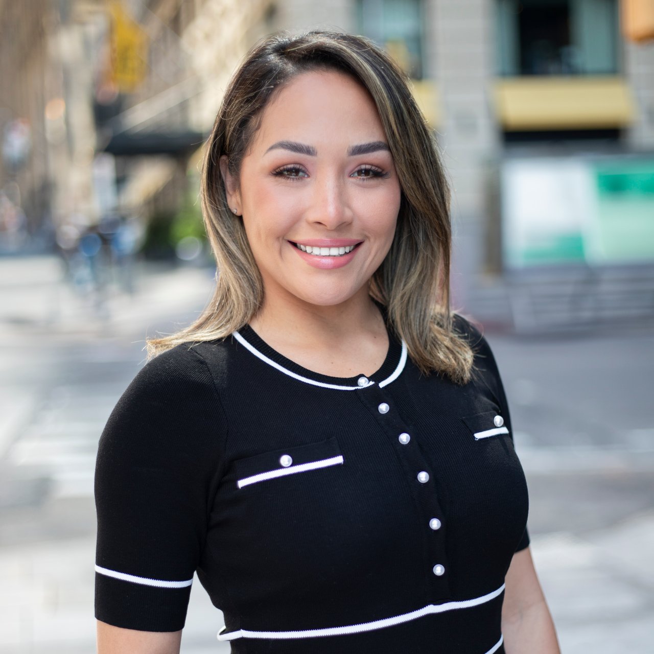 Diana Munoz smiling in a black top with white trim on a city sidewalk.