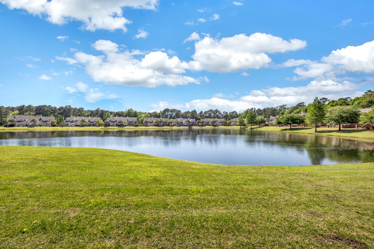 Lakefront homes across calm water, seen beyond a broad grassy shoreline.