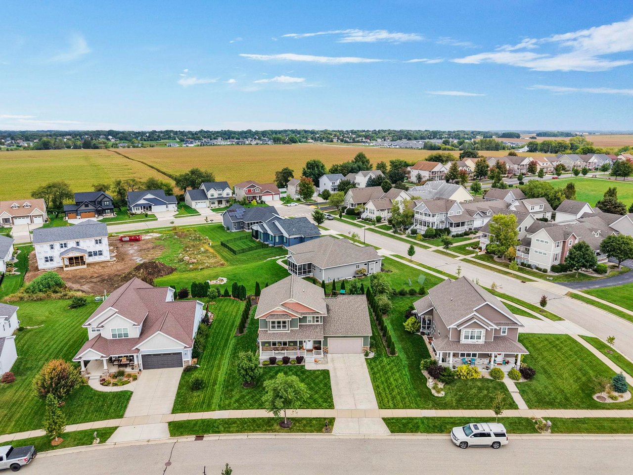 Aerial drone view of a well-maintained residential neighborhood in Sun Prairie, Wisconsin, featuring spacious single-family move-up homes with manicured lawns, sidewalks, and open green fields in the distance.
