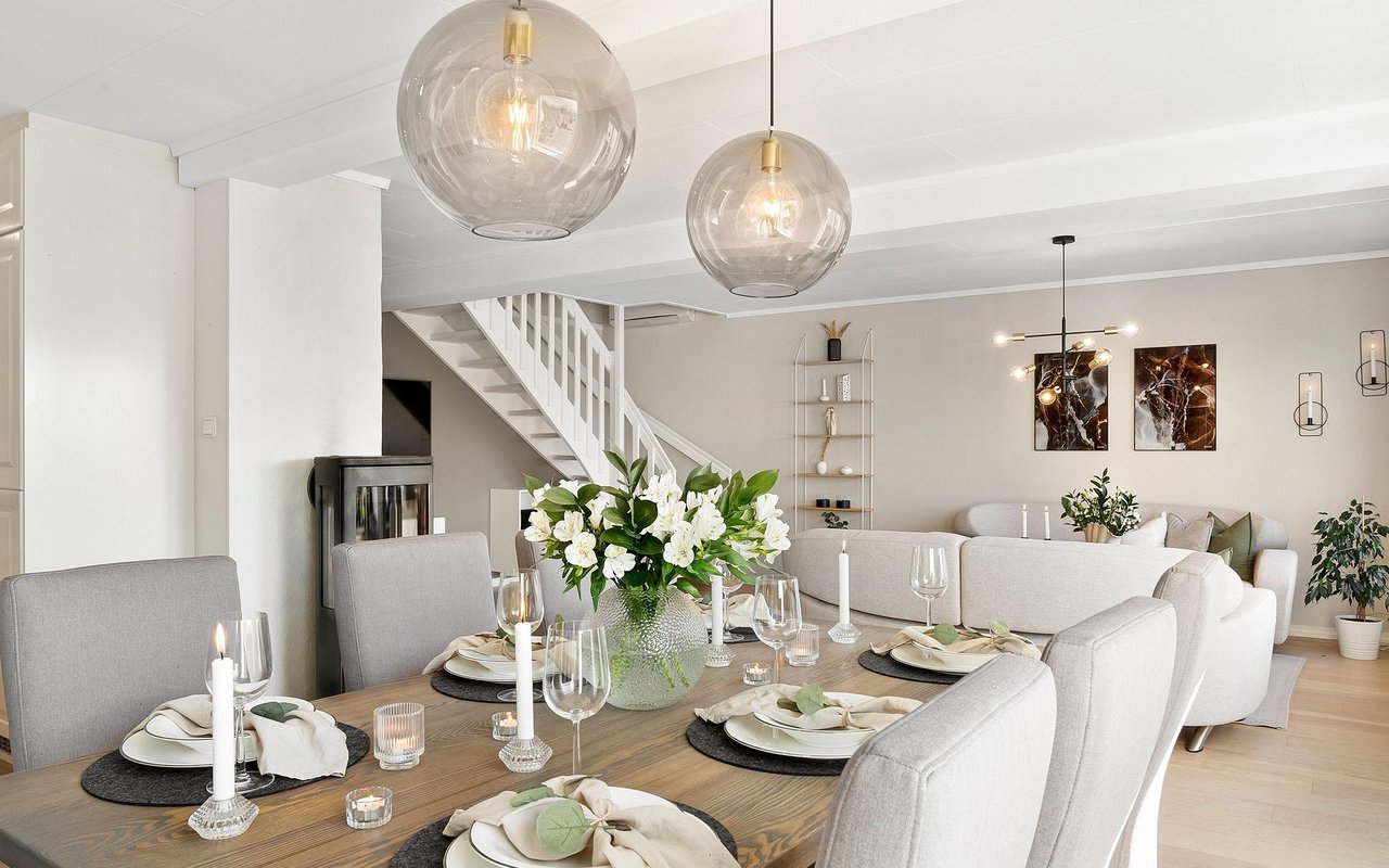 Staged dining and living room with a set table, glass pendant lights, and a staircase.