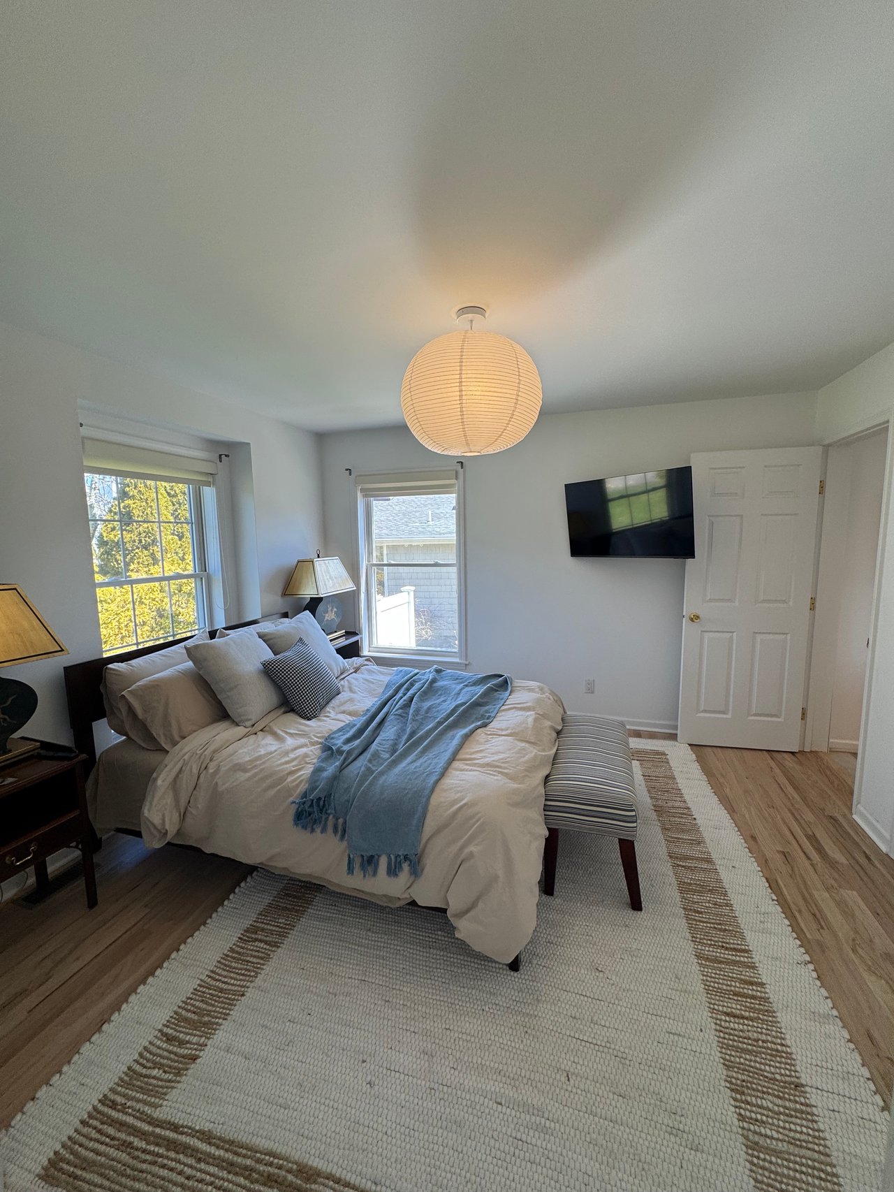 Bedroom with a white bed, blue throw, striped bench, and round paper lantern.