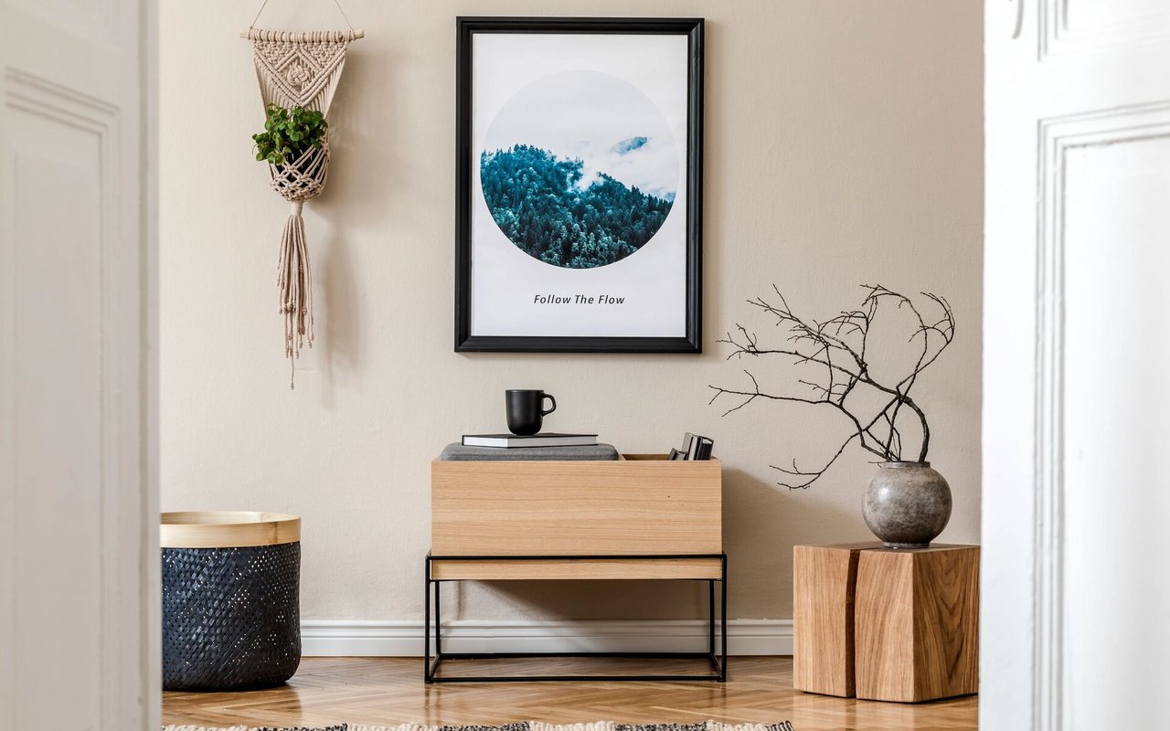 Staged interior with a wood console, framed forest print, hanging plant, and branch arrangement.