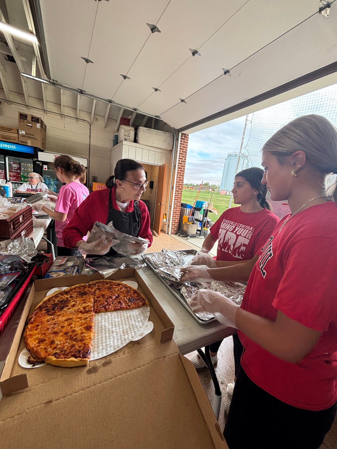 Hinsdale Central volunteers wrap food at a concession stand beside an open box of cheese pizza.