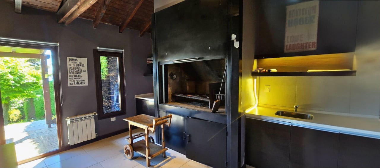 Kitchen with a large built-in barbecue, yellow-lit counter, and open doors to a leafy garden.
